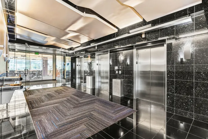 Polished black tile flooring, stainless steel elevator doors, black speckled wall tiling, glass partition walls, and integrated ceiling lighting