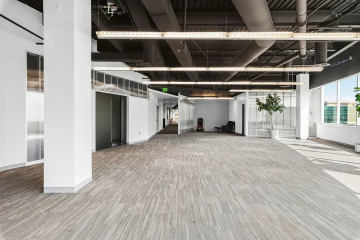 Expansive open floor plan with polished wood-finish flooring throughout, abundant natural light from floor-to-ceiling windows, and soaring ceilings with exposed structural elements