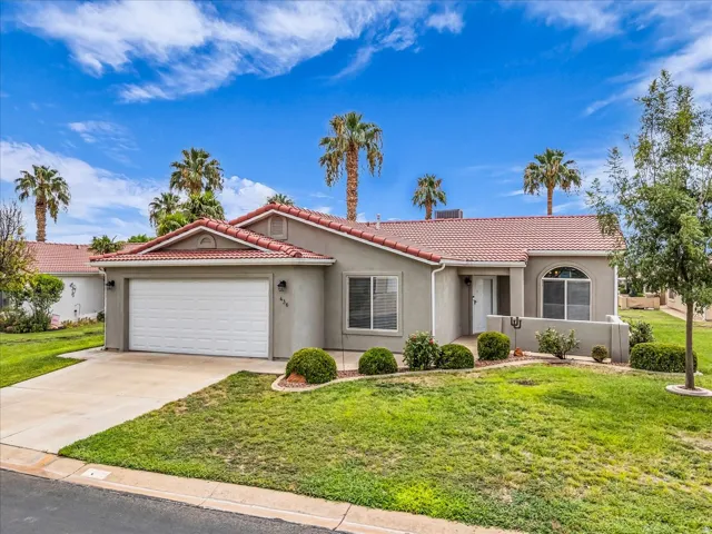 Single-story residence featuring a stucco exterior with a clay tile roof, two-car garage, and manicured front lawn with mature palm trees and drought-resistant landscaping