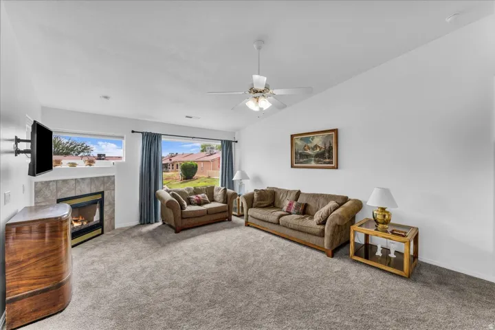 Carpeted living area featuring a tiled fireplace, large window with outdoor visibility, and a ceiling fan