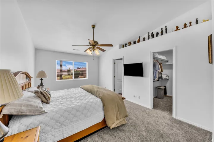 Vaulted ceiling with a ceiling fan, window with horizontal blinds, built-in display shelf, and an open closet with shelving