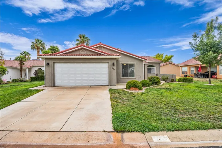 Stucco exterior with a tile roof, an integrated garage, a concrete driveway, and established landscaping