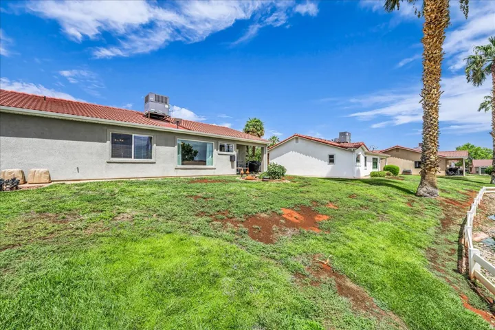 Red tile roof, stucco exterior, multiple windows, established palm trees, white perimeter fencing
