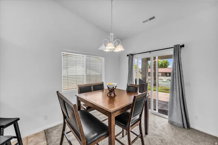 Vaulted ceiling, sliding glass patio door, window with blinds, overhead chandelier, and carpet flooring