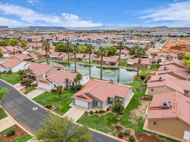 Residential community with a central pond featuring a fountain, surrounded by properties with tile roofs and mature palm trees