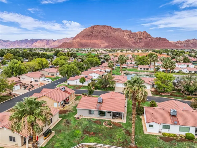 Expansive residential development with red tile roofs and mature palm trees, featuring a serene water element, framed by distant red rock mountains