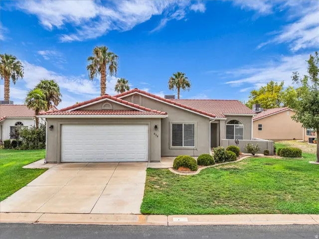 Single-story residence featuring a stucco exterior with a clay tile roof, two-car garage with white paneled door, and mature landscaping including palm trees and shrubs