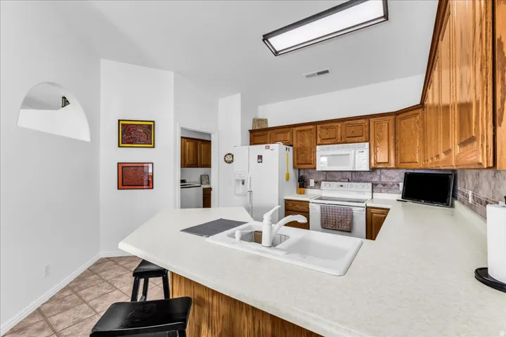 Kitchen featuring wood-finish cabinetry, white appliances, and a tiled backsplash