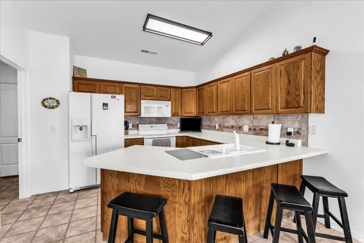 U-shaped kitchen with wood-finish cabinetry, tile flooring, and white countertops