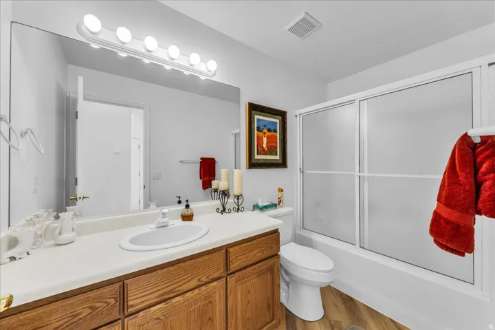 Wood-finish flooring, full vanity mirror, integrated vanity sink, wood-finish cabinetry, and a shower-tub combination with frosted sliding doors