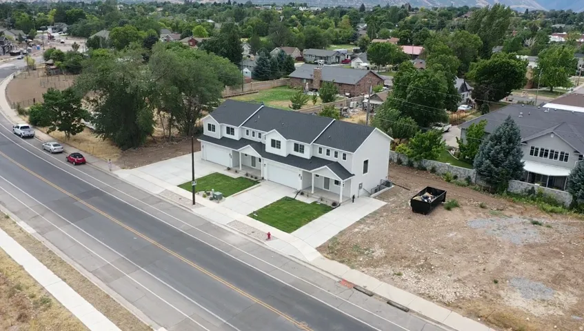 Newly constructed residential building with a dark shingle roof, light-colored siding, and attached garages