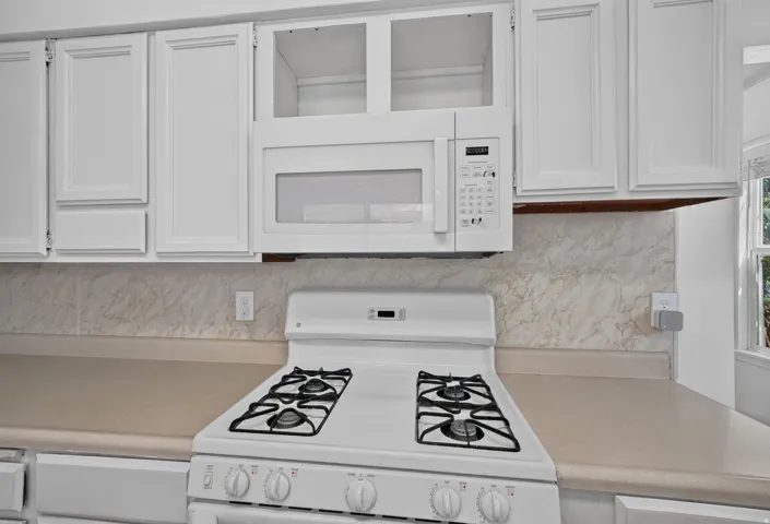 White cabinetry, integrated microwave, durable countertop, gas range, and a patterned backsplash