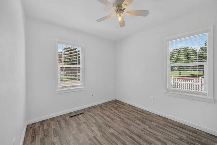Wood-finish flooring, white walls, two windows with blinds, and a ceiling fan with integrated lighting