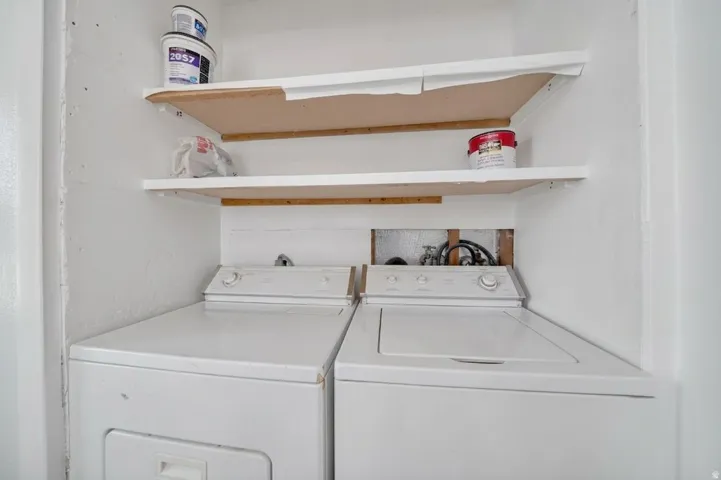 Dedicated laundry closet featuring side-by-side washer and dryer units, white wood-finish shelving with wood-tone accents, and ample storage for household essentials and supplies