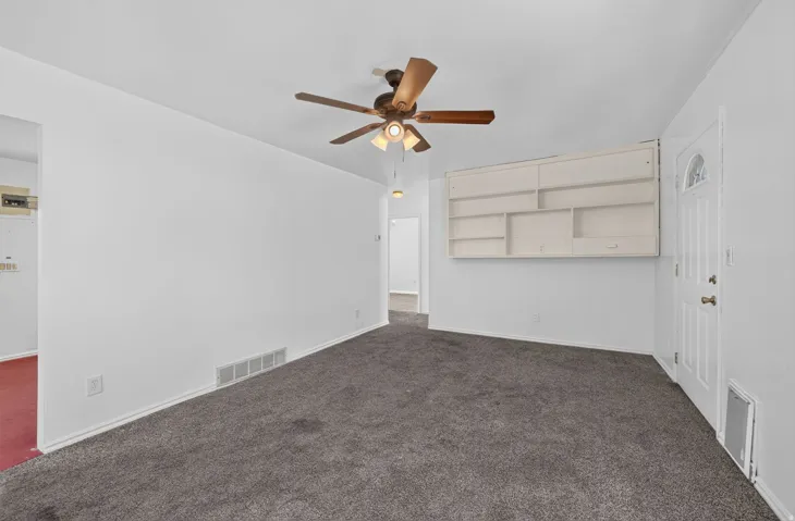 Neutral wall finish, ceiling fan with integrated lighting, built-in wall shelving, paneled entry door, and gray carpeting