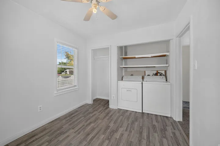 Wood-finish flooring, ceiling fan, window with blinds, built-in shelving, and integrated laundry appliances