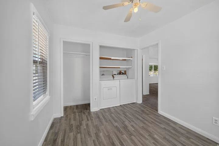Wood-finish flooring, built-in shelving, ceiling fan, and window with blinds