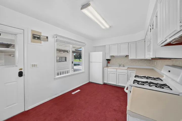 Kitchen featuring white cabinetry, a white refrigerator, a gas range, a single basin sink, and a light-toned countertop