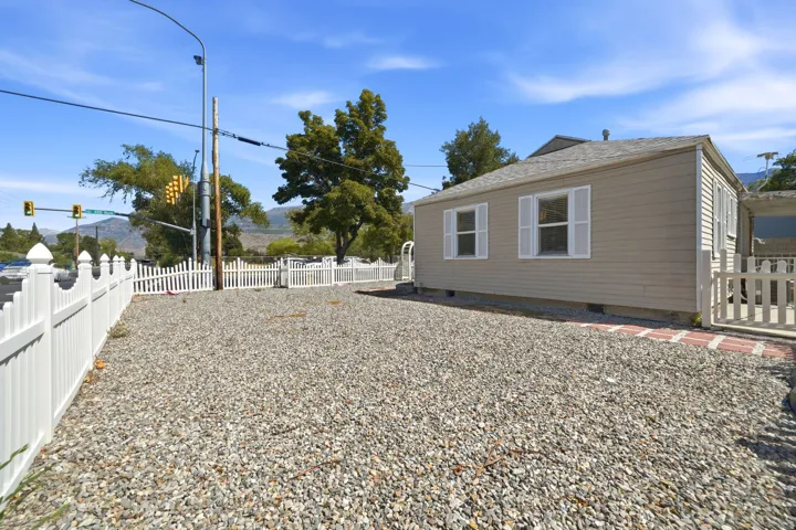 Charming single-story residence with board-and-batten siding and dual windows, situated on a generous gravel lot enclosed by white picket fencing