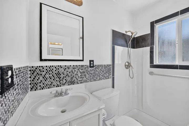 Bathroom featuring a vanity with an integrated sink, mosaic tile backsplash, framed mirror, and a shower with a single-handle faucet and a window
