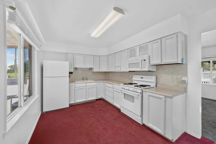 White cabinetry, white appliances, light-colored countertops, overhead fluorescent lighting, and a large window