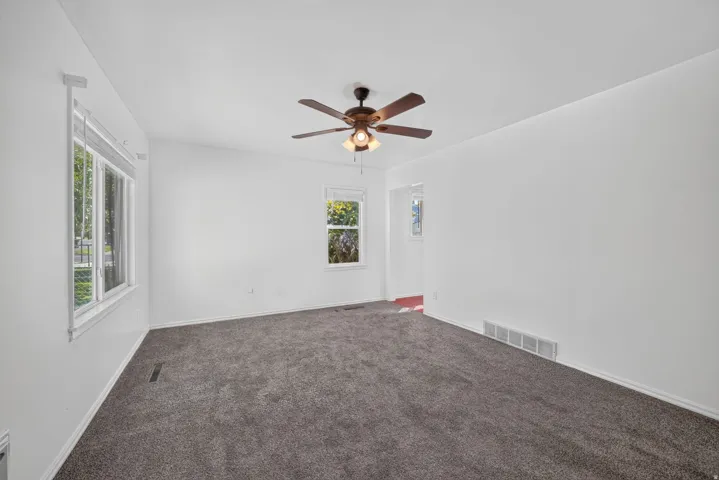 Spacious room featuring gray carpeting, a ceiling fan with integrated lighting, and multiple windows
