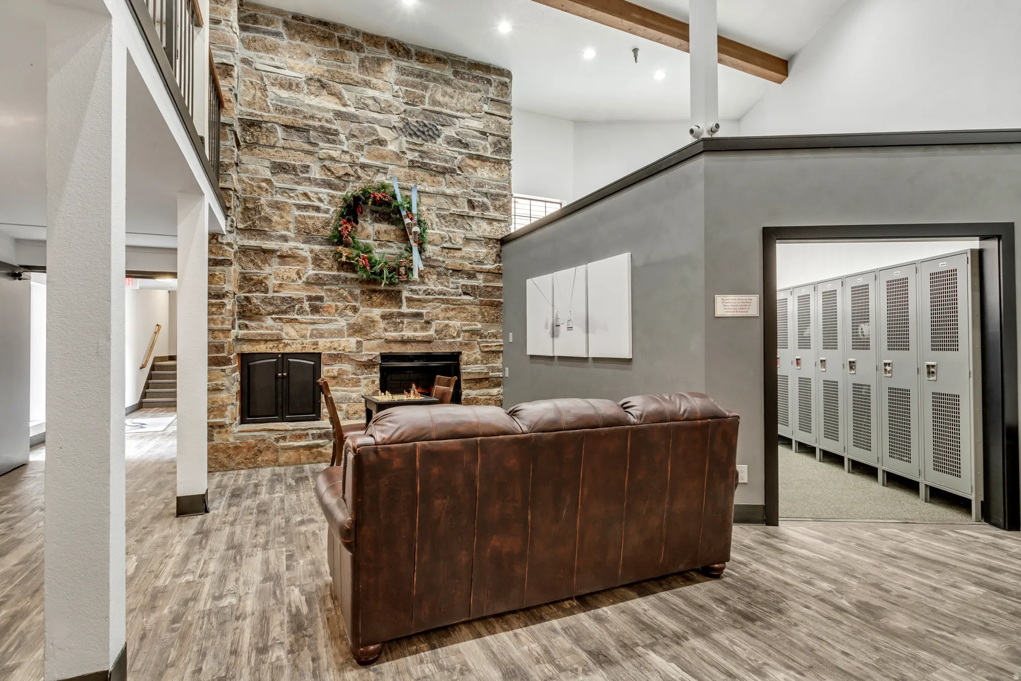 Floor-to-ceiling stone fireplace, wood-finish flooring, vaulted ceilings with exposed beams, open doorway to locker storage