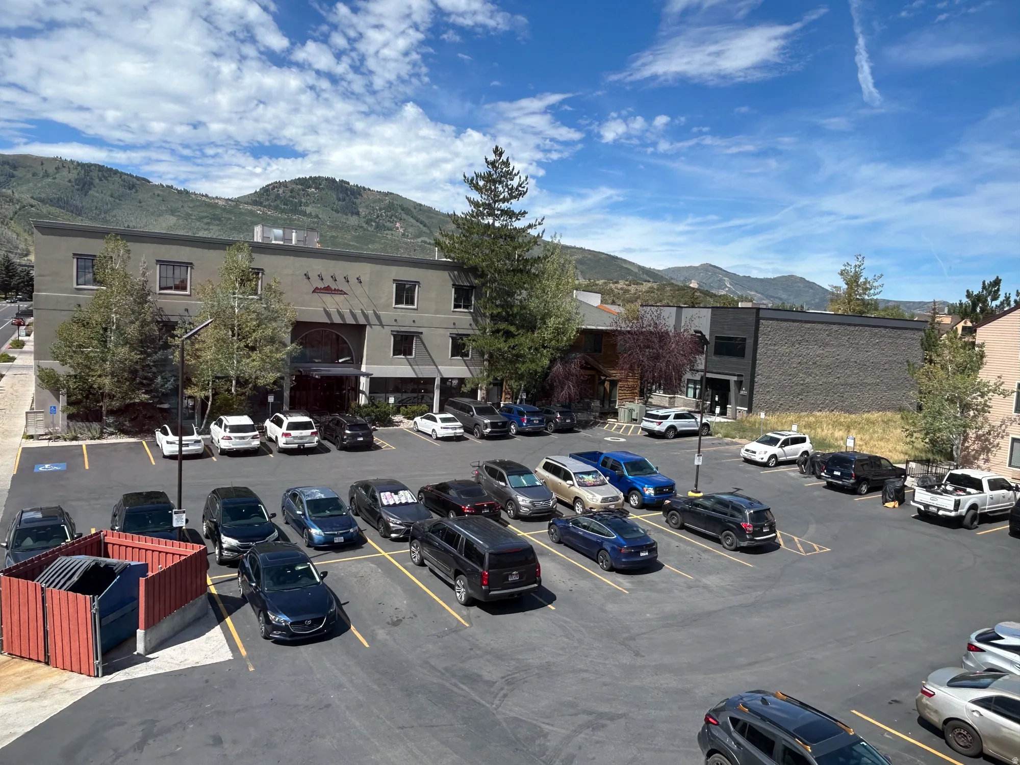 Expansive paved parking area accommodating numerous vehicles, bordered by a multi-story building with multiple windows