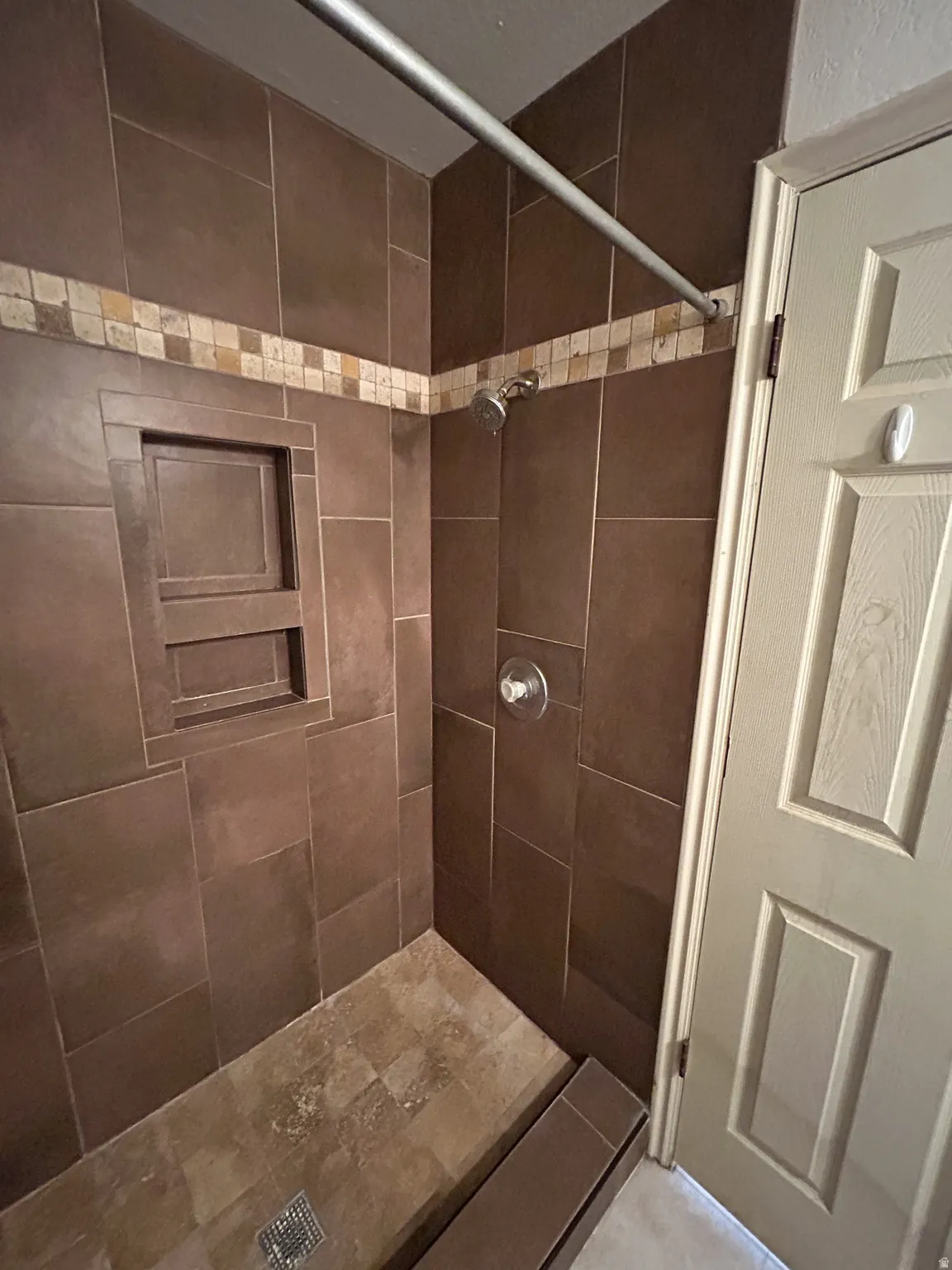 Tiled shower enclosure featuring a recessed niche, an accent tile band, a shower head, and a single-handle temperature control