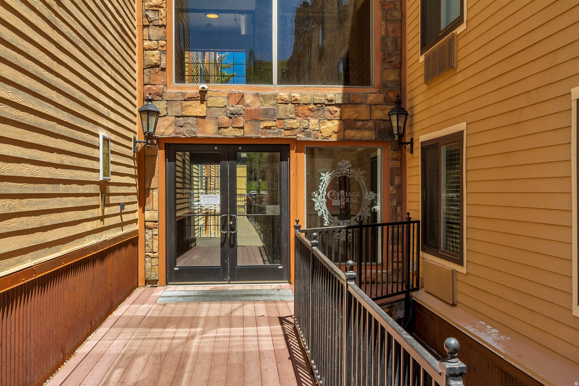 Entryway featuring stone accents, wood-finish siding, double glass doors, and a black wrought iron railing