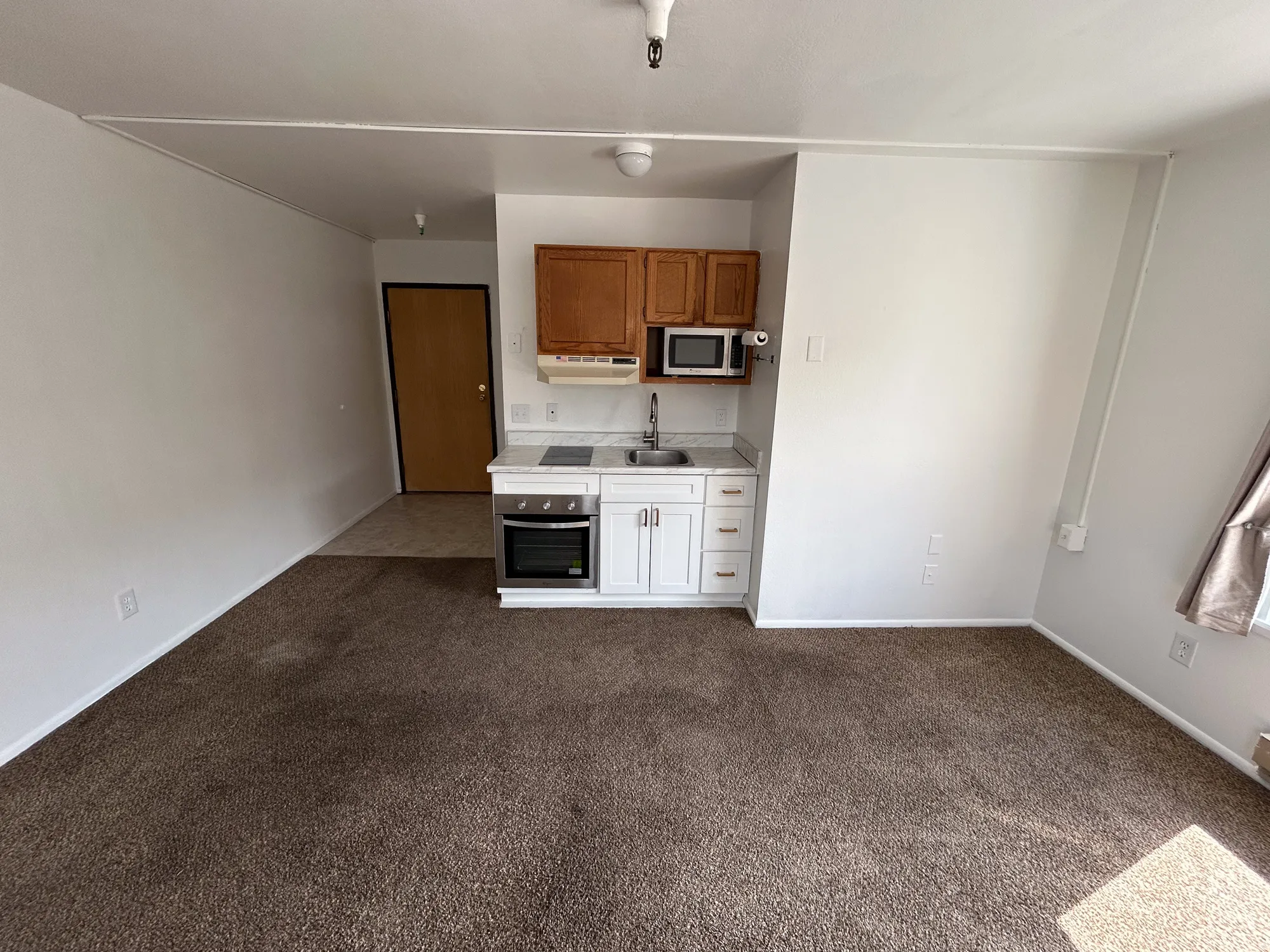 Compact kitchen area featuring wood cabinetry, white base cabinets, a built-in microwave, an integrated cooktop, and an under-counter oven