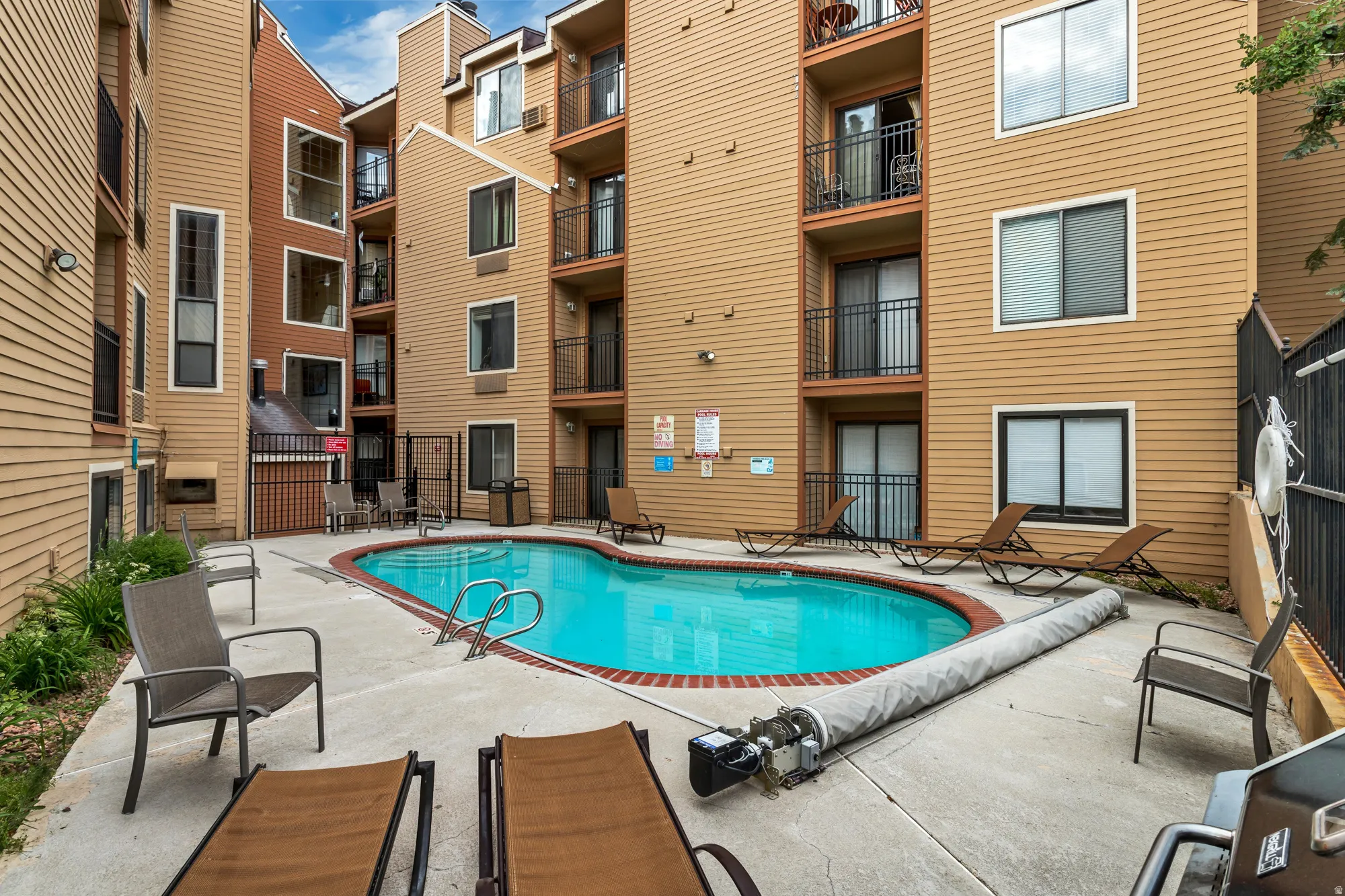 Resort-style swimming pool with lounge seating and concrete decking, surrounded by multi-story residential buildings featuring siding exteriors and balconies