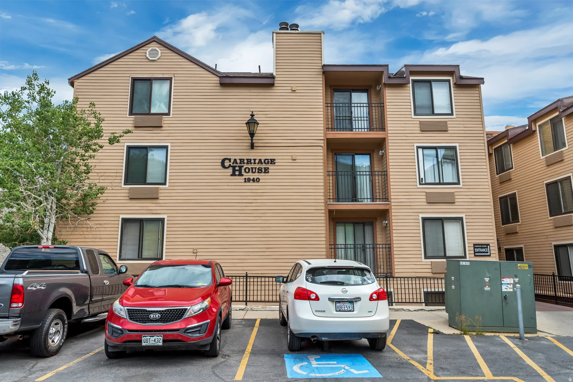 Multi-story building with tan siding, multiple balconies with black railings, and a prominent "Carriage House" sign