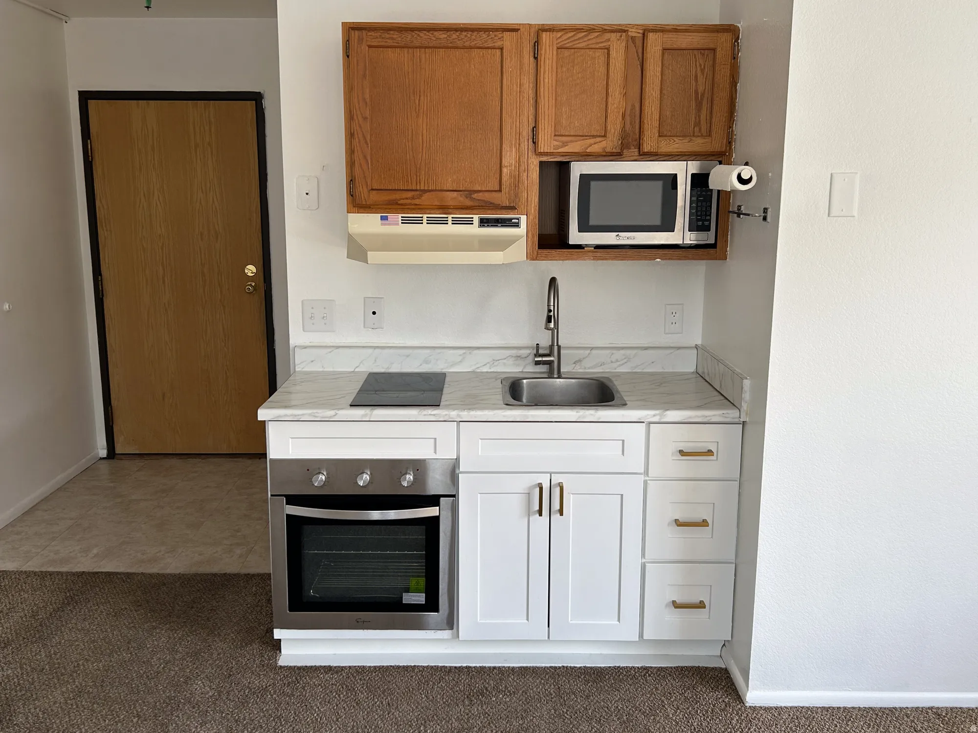 Compact kitchen featuring white cabinetry, a built-in oven, a stainless steel sink, and a built-in microwave
