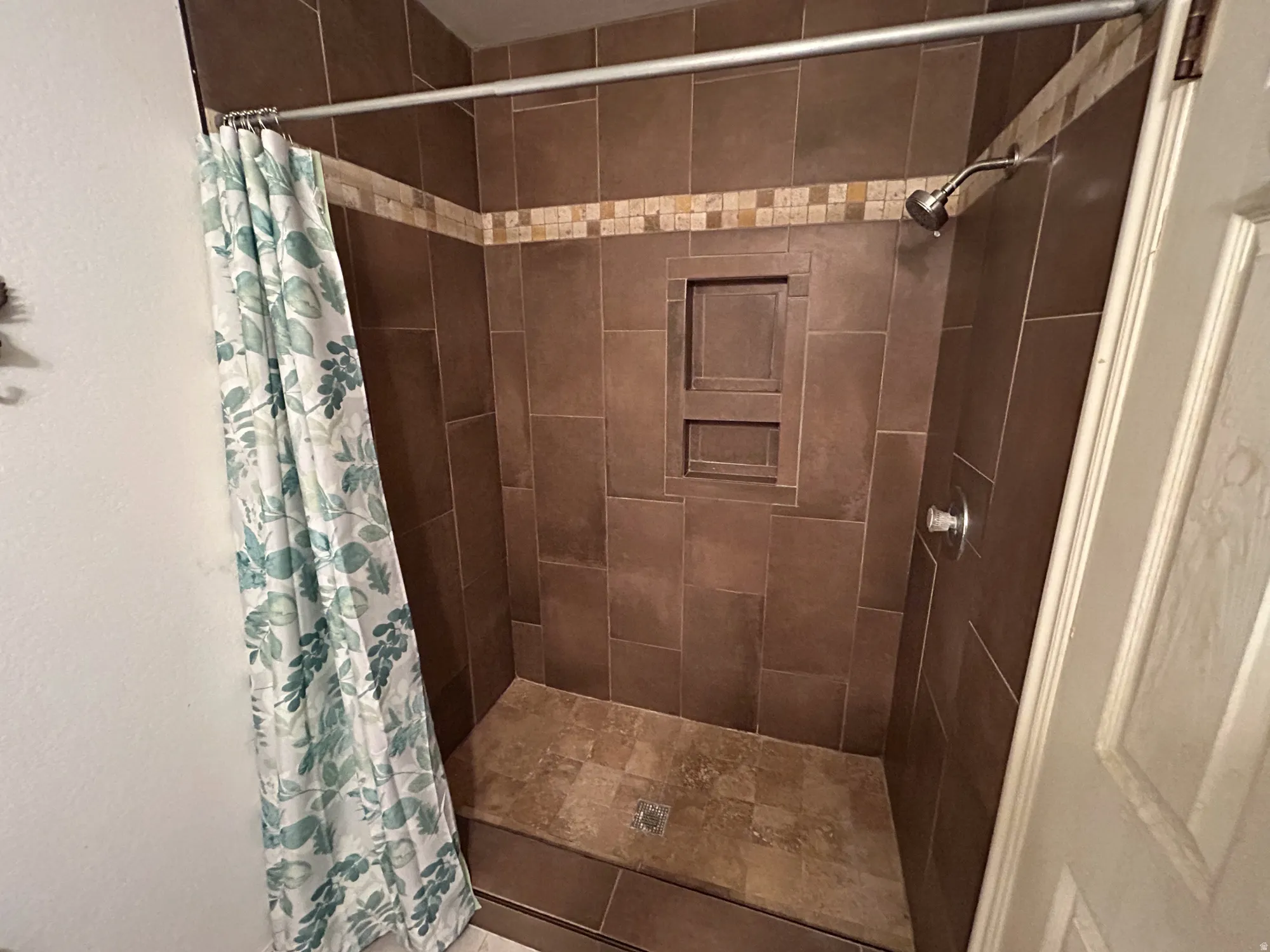 Tiled shower enclosure featuring a mosaic accent band, recessed shelving, and a tiled shower pan