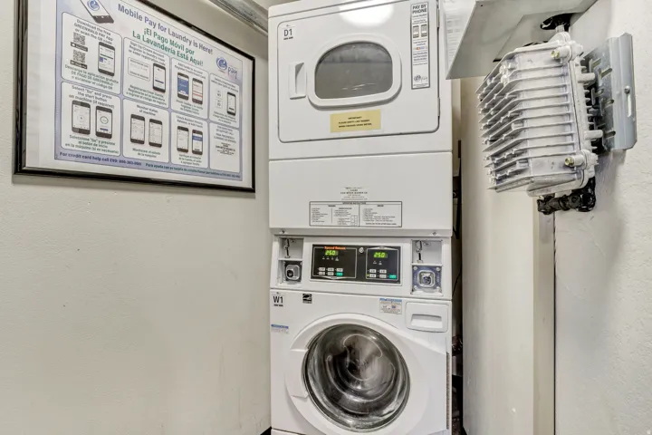 In-Unit Laundry featuring stackable washer and dryer with digital controls, complemented by wall-mounted drying rack and instructional signage for convenient laundry management