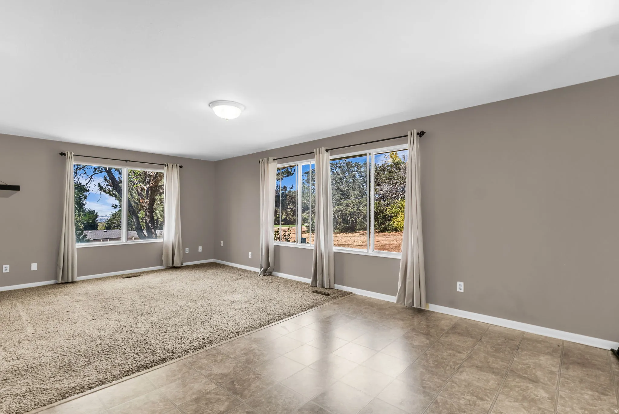 Spacious living area featuring neutral-toned walls, abundant natural light from multiple windows, and a combination of carpet and tiled flooring