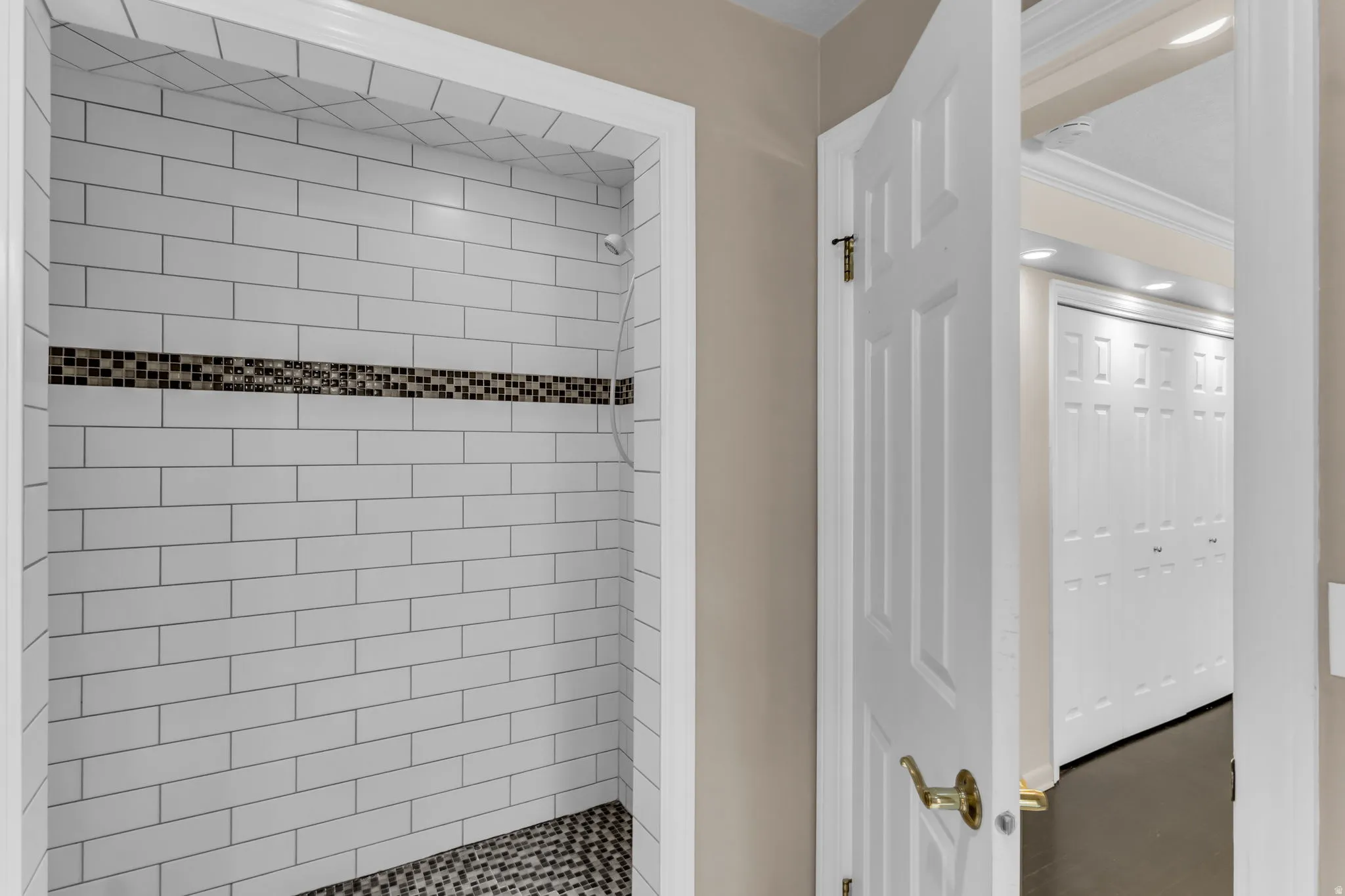 Shower enclosure featuring white subway tile, a mosaic tile accent band, and a dark pebble-style floor