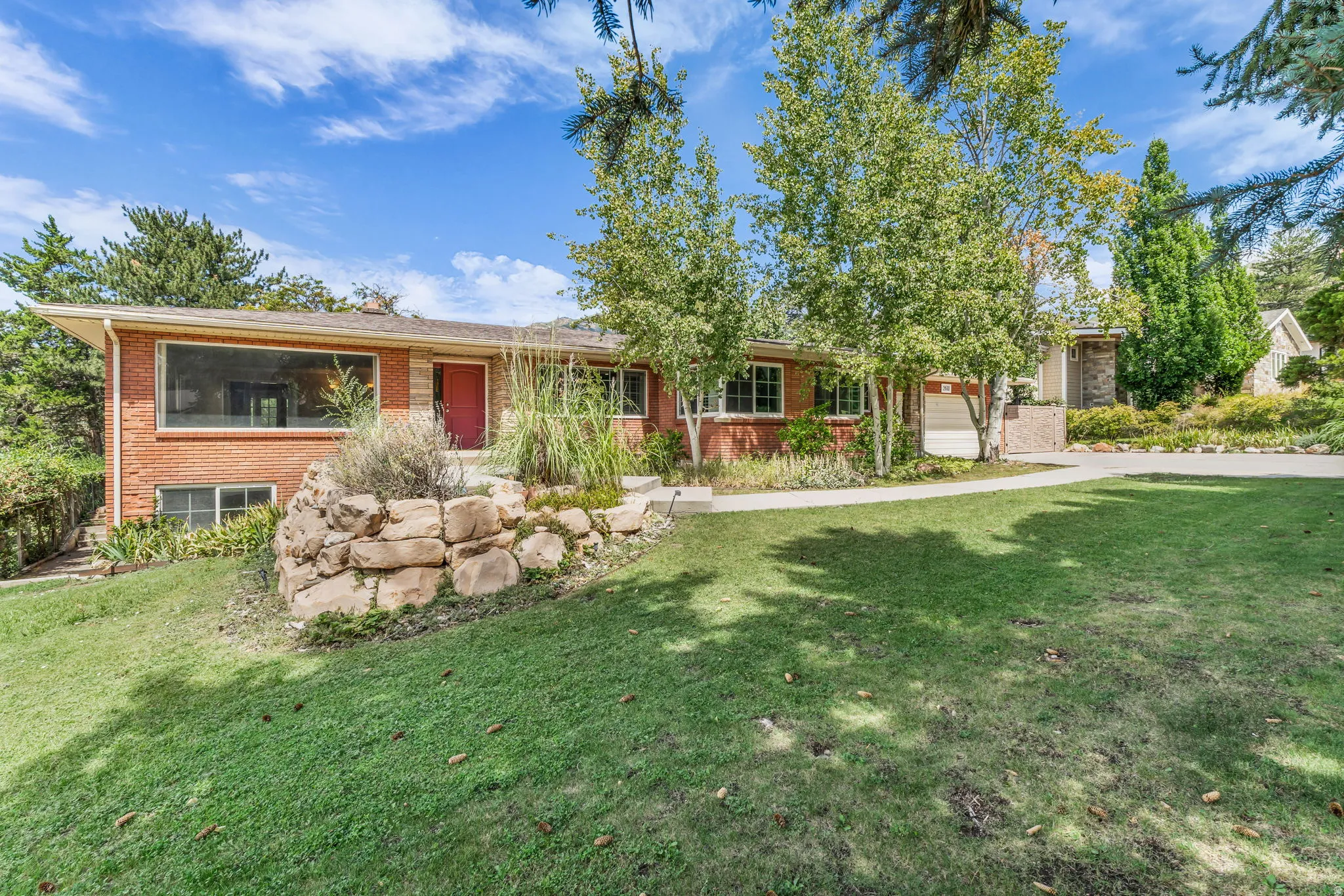 Brick exterior with a red front door, featuring a stone retaining wall and a concrete driveway