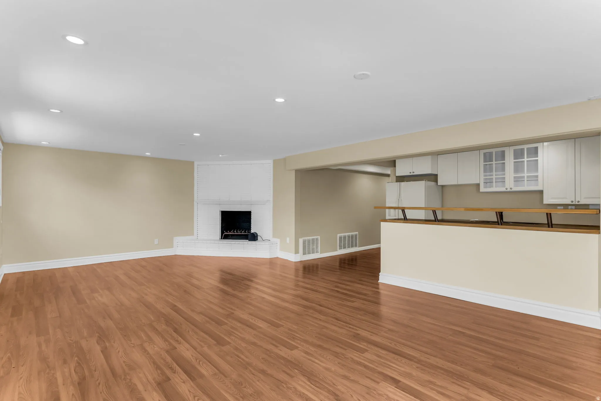 Expansive room with wood-finish flooring, recessed lighting, and a white brick fireplace