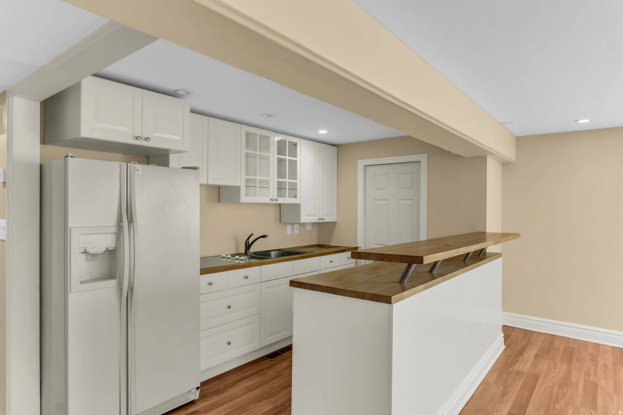 Kitchenette with white cabinetry, wood-finish countertops, stainless steel sink, and wood-finish flooring