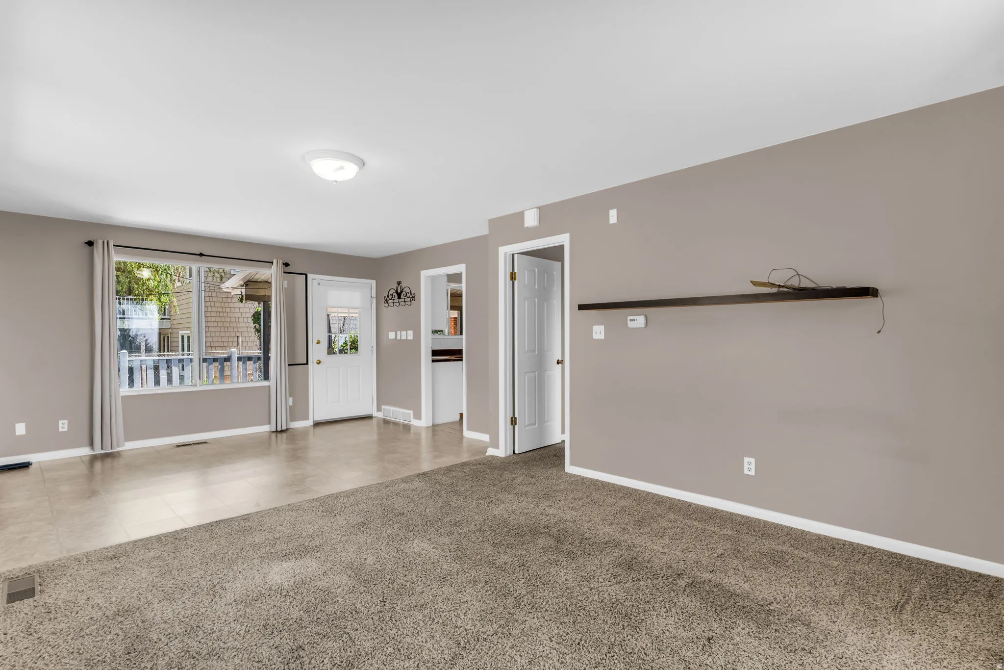 Spacious living area featuring neutral-toned walls, a large picture window, and a combination of carpet and tiled flooring