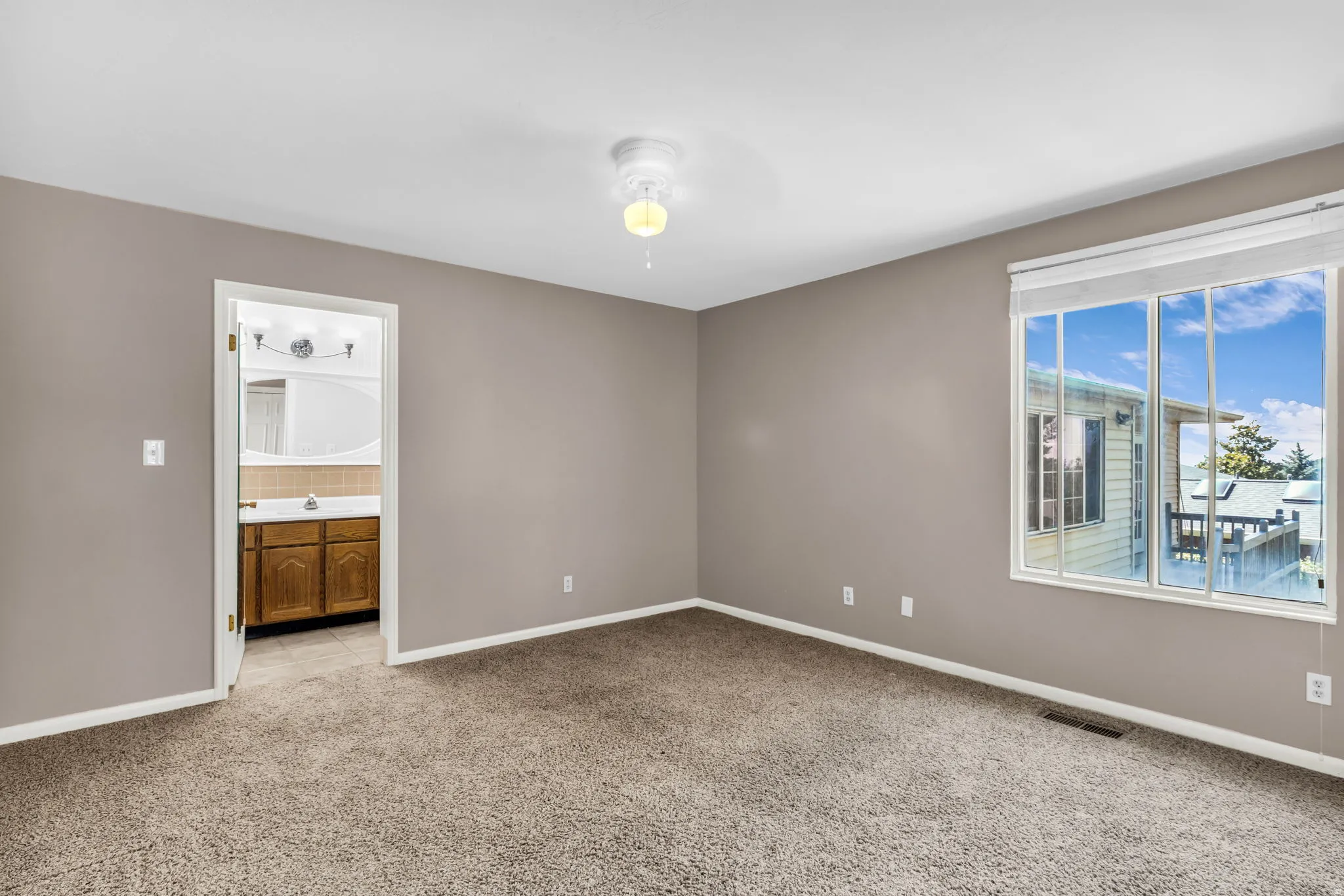Spacious room with plush carpet flooring, a large window, and a ceiling fan
