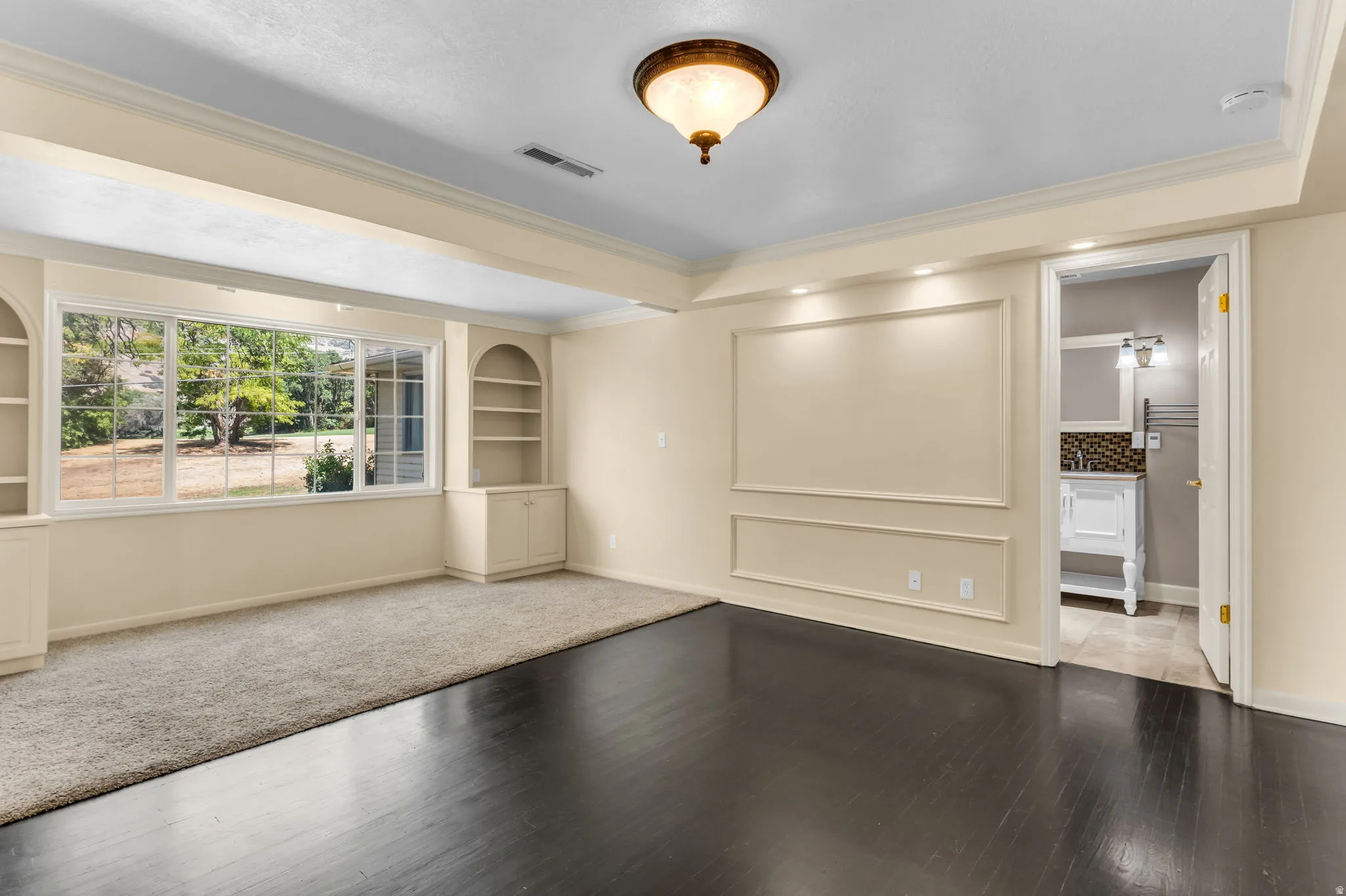 Hardwood-style flooring with a recessed carpet area, custom built-in shelving, large multi-pane windows, decorative wall molding, and crown molding