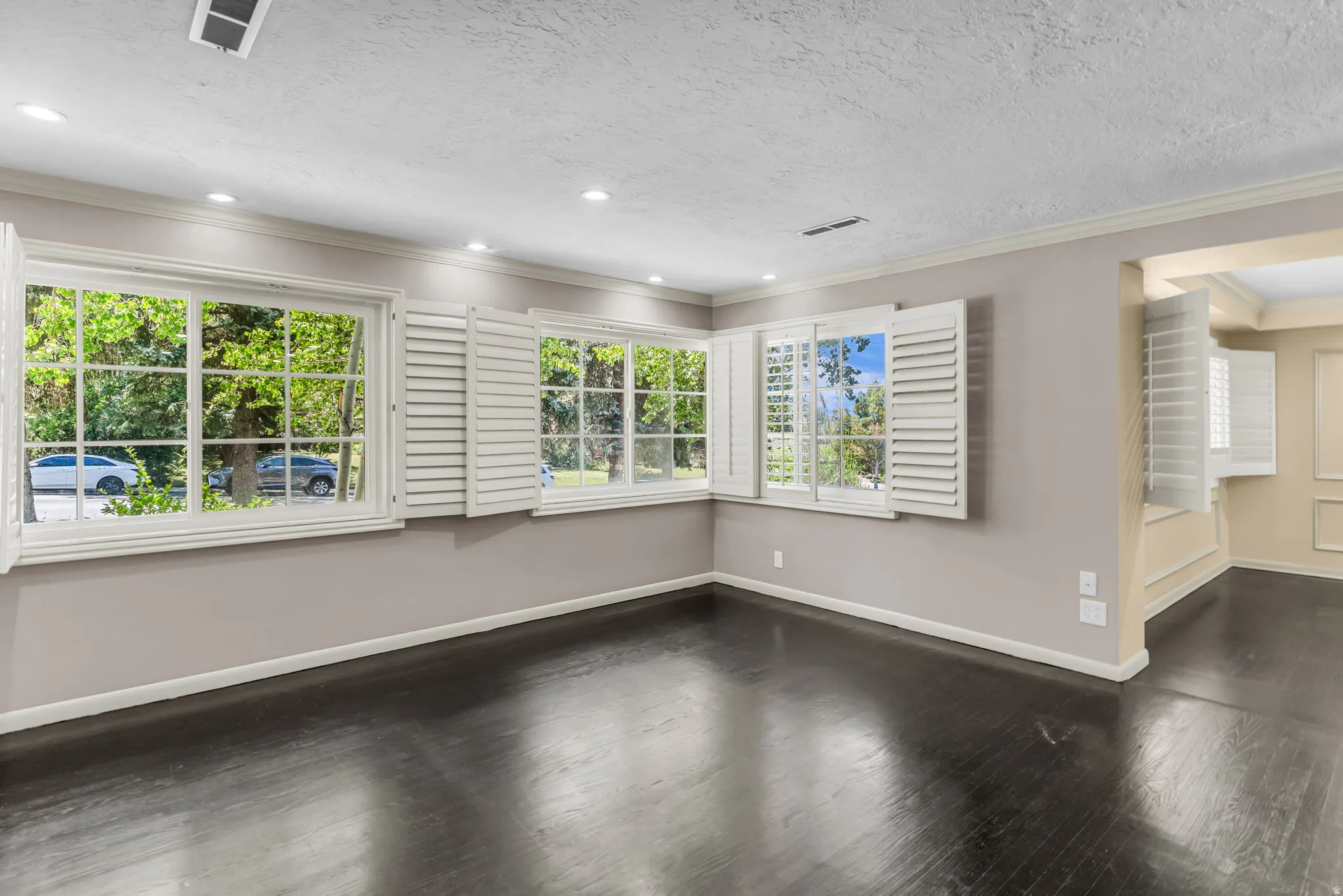 Dark wood-finish flooring, recessed lighting, white louvered window shutters, and white crown molding