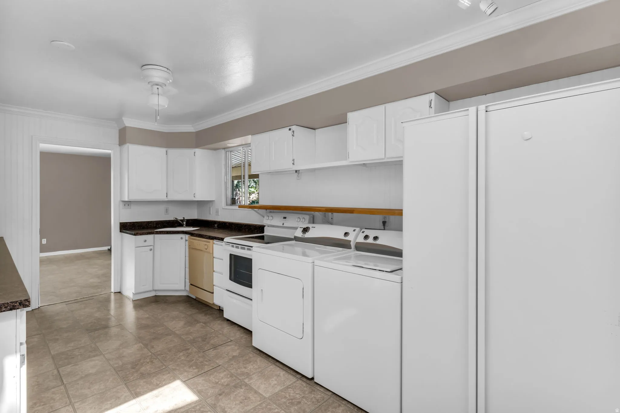 Full kitchen with white cabinetry, dark countertops, tiled flooring, and laundry appliances