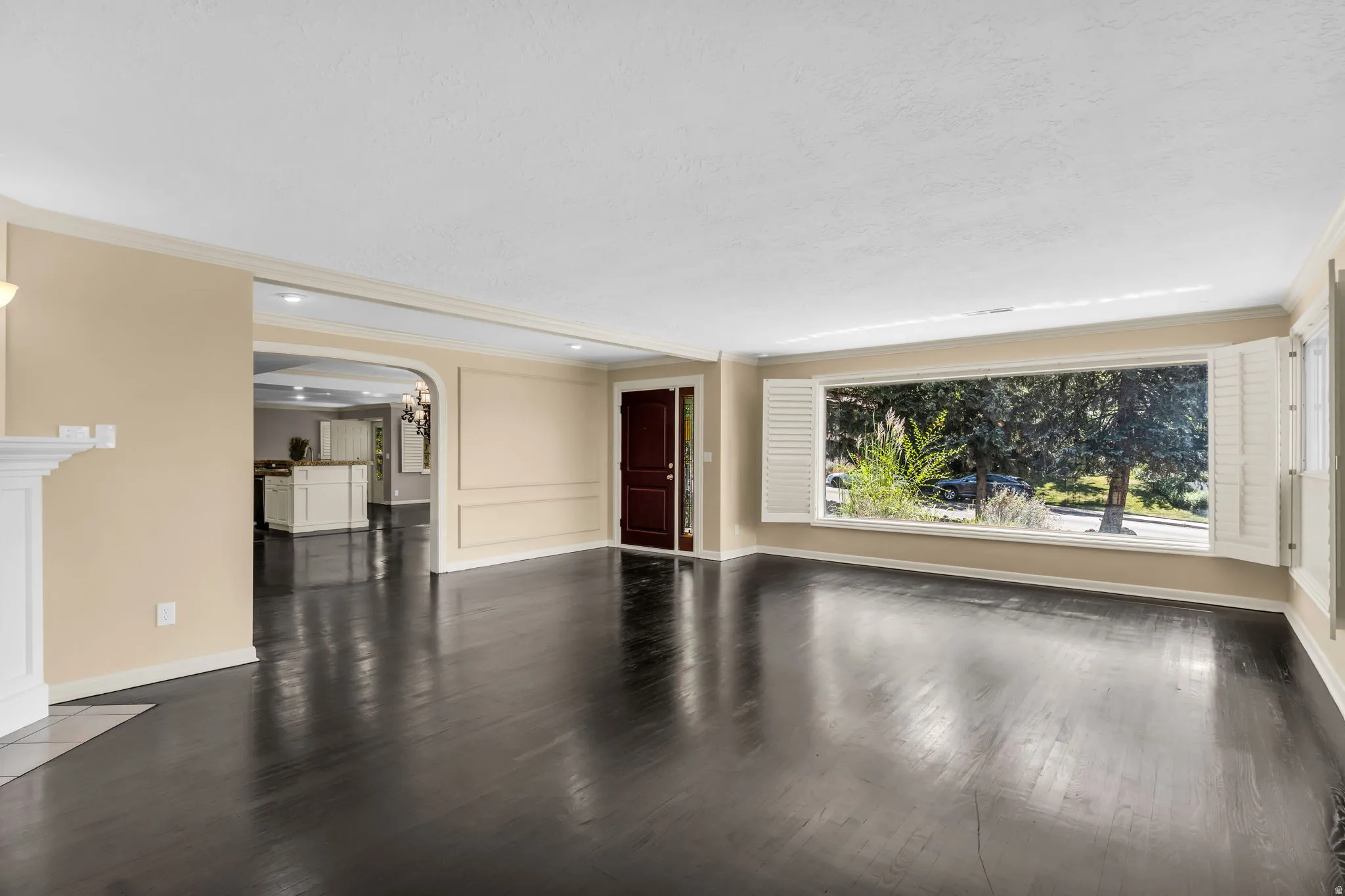 Dark wood-finish flooring, white fireplace mantel, arched doorway, and a large bay window with plantation shutters