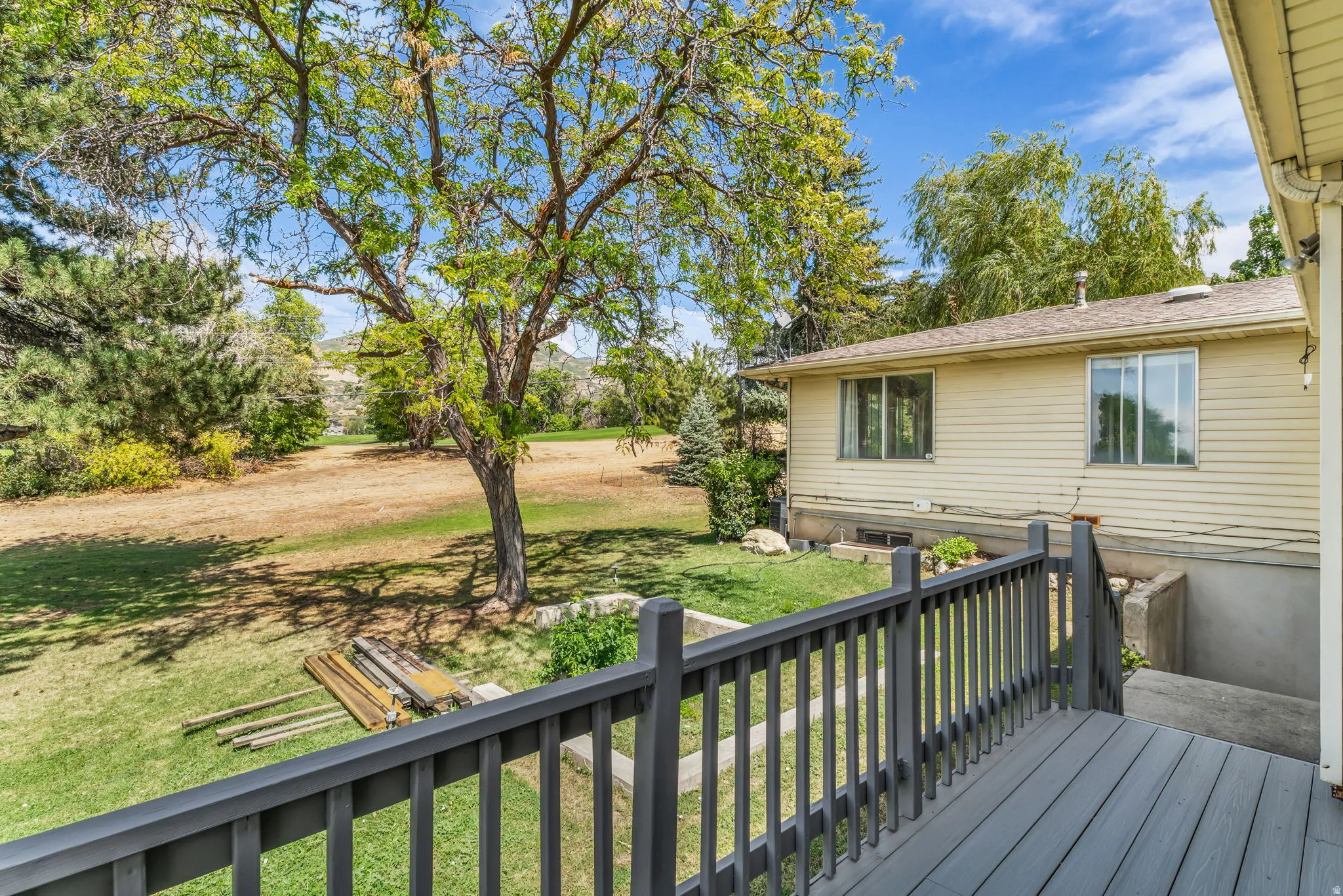 Exterior deck with wood-finish railing, vinyl siding, and a sloped backyard with mature trees