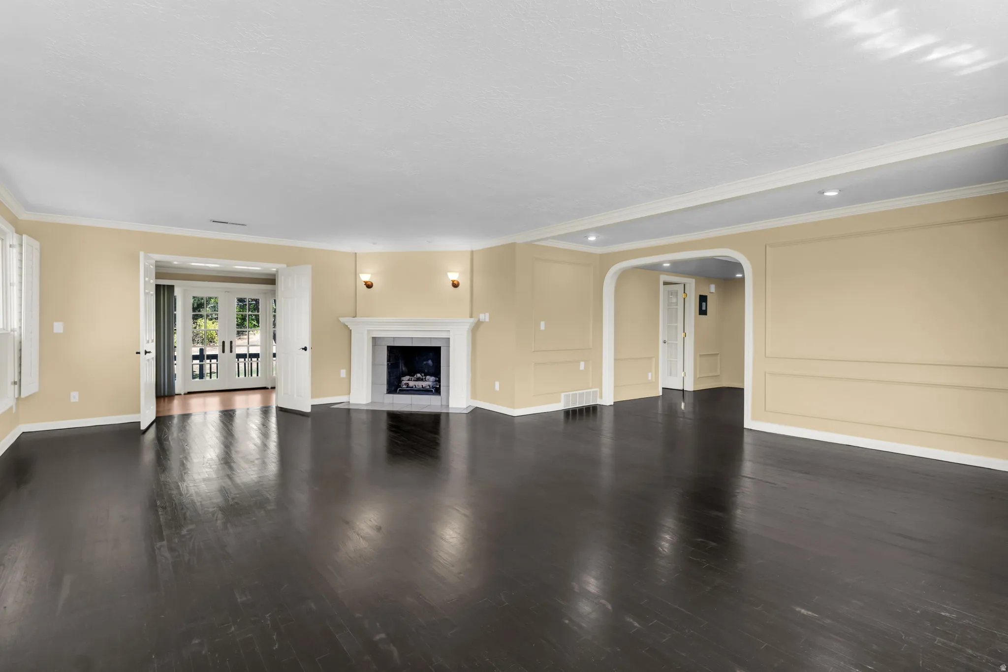 Dark wood-finish flooring, a traditional fireplace with a mantel, recessed lighting, wall sconces, and an arched entryway
