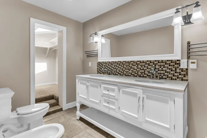 Dual vanity with white cabinetry and integrated sinks, mosaic tile backsplash, and a large framed mirror